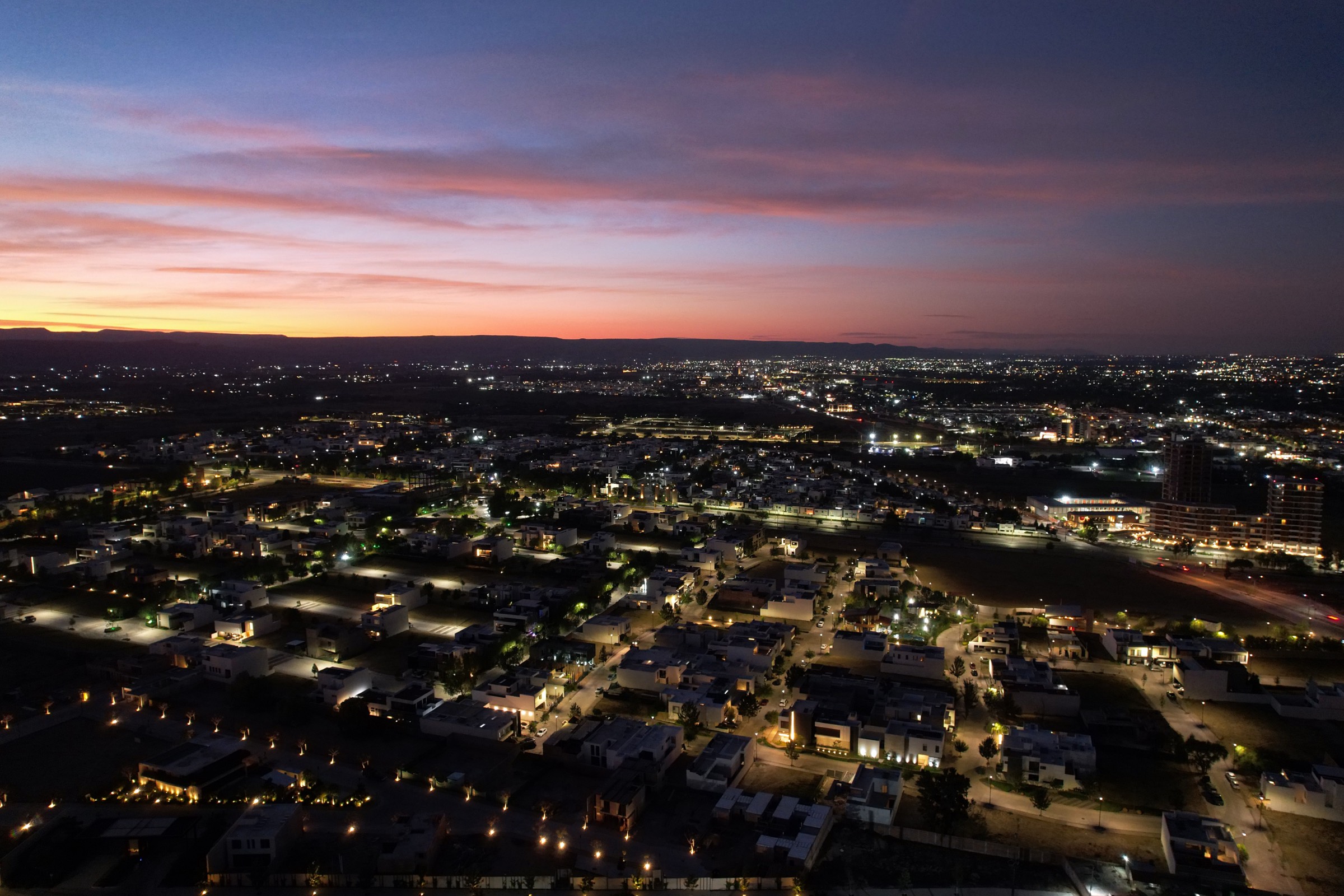 Vista aérea al anochecer de un desarrollo habitacional con la ciudad al fondo.