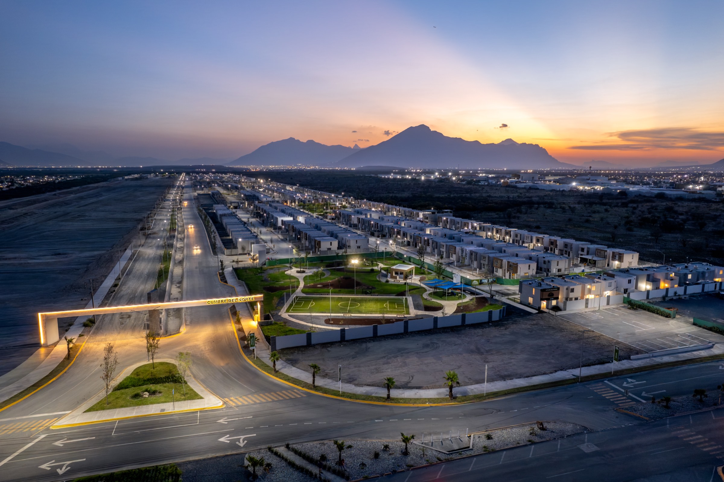 Vista aérea al atardecer de un desarrollo habitacional terminado junto a la reserva territorial en obra.